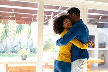 Happy african american couple standing next to window, embracing and smiling
