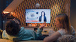 © Framestock - Couple sitting on sofa in living room, looking at each other, watching TV news about poliovirus and water pollution. Man and woman spending weekend at home together. TV live broadcasting.
