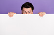 Photo portrait of nice young man playing hide and seek behind white poster look blank space isolated on purple color background