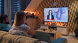 © Framestock - Couple sitting on sofa in living room with snacks, talking, watching IT TV news about presentation of new digital gadget, VR goggles. Spending weekend together at home. TV live broadcasting. Metaverse
