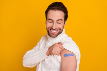 Poster - Photo of charming funny guy wear white pullover looking vaccination sticky plaster patch isolated yellow color background