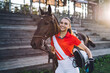 Happy horsewoman holding horse with reins and smiling