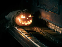 Halloween Pumpkin Lantern With Scary Face Glowing Inside Under Shawl On An Old Piano.