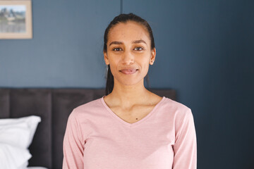 Portrait of happy biracial woman smiling to camera in bedroom