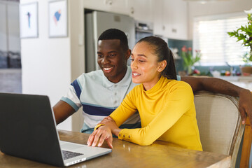 Wall Mural - Happy diverse couple making video call on laptop smiling and talking to screen in kitchen