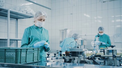 Women work on the capsule packaging line and put the finished product into a box. Bottle filling machine. Bottles on a conveyor belt. Production line of pharmaceutical manufacturing