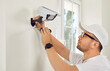 © Studio Romantic - Technician with screwdriver and smart glasses installs security remote camera with LED light on wall in white office or medical clinic. Security and privacy round the clock control.