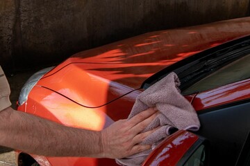 Wall Mural - Closeup of a male hand cleaning his red car with a rag