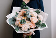 Very nice young woman holding big and beautiful bouquet of fresh roses, carnations, eucalyptus flowers in pastel pink colors, cropped photo, bouquet close up