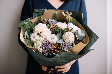 Very nice young woman holding big and beautiful winter bouquet of fresh Nobilis spruce, pine cones, carnations, cotton, cropped photo, bouquet close up