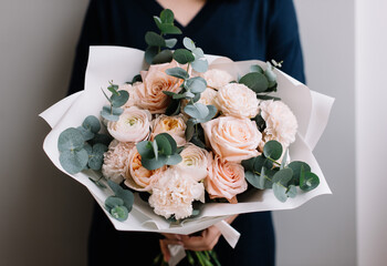 Wall Mural - Very nice young woman holding big and beautiful bouquet of fresh roses, carnations, eucalyptus flowers in pastel pink colors, cropped photo, bouquet close up