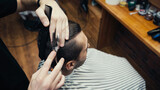 Overhead view of barber cutting hair of man in blurred hairdressing cape in barbershop.