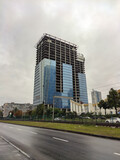 Fototapeta Miasto - A huge unfinished skyscraper with glass walls on the background of an asphalt road