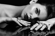 © Rytis - Fashion and make-up concept. Studio portrait of beautiful woman with fancy make-up and many various rings on her fingers lying on dark glass surface. Model looking at camera. Black and white image