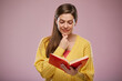© Yuriy Shevtsov - School teacher reading open book and touching chin. Isolated advertising portrait on pink back.