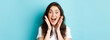 © Mix and Match Studio - Close up of excited young woman holding hands near face, gasping and looking amazed at camera, stare surprised at super cool news, standing over blue background