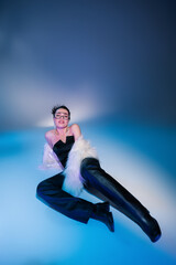 Wall Mural - seductive model in black leather pants and white fluffy jacket lying on blue background.