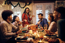 Happy Black Woman Holding Toast During Thanksgiving Meal With Friends At Dining Table.