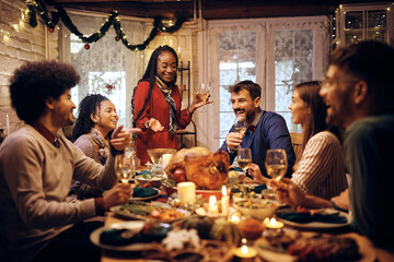 Wall Mural - Happy black woman holding toast during Thanksgiving meal with friends at dining table.