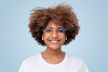 Wall Mural - Portrait of smiling african student girl in white t-shirt and trendy glasses on blue background