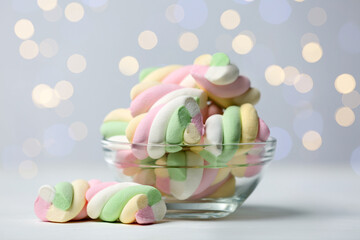 Wall Mural - Glass bowl with colorful marshmallows on white table against blurred lights, closeup