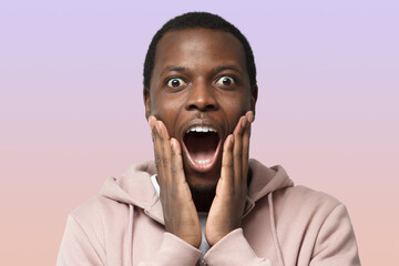 Casual dressed young african man in pink hoodie shouting oh my god with open mouth