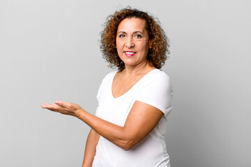 middle age hispanic woman smiling cheerfully, feeling happy and showing a concept in copy space with palm of hand