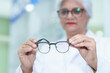 © ND STOCK - Middle aged ophthalmologist holding eyeglasses and examining them, focus on eyeglasses, close-up