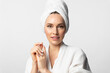 Beautiful woman with perfect skin in a bathrobe and towel over her head looks at the camera on a white background. Cosmetic concept.