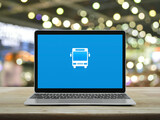 Fototapeta Panele - Bus flat icon on modern laptop computer monitor screen on wooden table over blur light and shadow of shopping mall, Business transportation online service concept