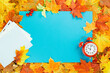 Autumn season. Yellow and bright maple orange autumn leaves flat lay on blue. Alarm clock, fall harvest time concept with mockup copy space. Foliage border frame background. Opening hours