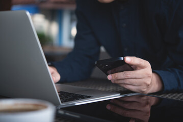 Canvas Print - Young smart business man using mobile phone and working on laptop computer at office. Male freelancer online working, surfing the internet at coffee shop