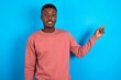 © Roquillo - young handsome man wearing pink sweater over blue background looking at camera indicating finger empty space sales