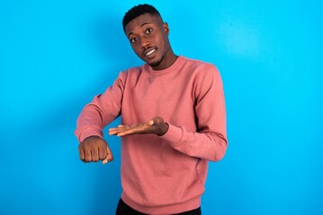 Wall Mural - young handsome man wearing pink sweater over blue background In hurry pointing to watch time, impatience, upset and angry for deadline delay.