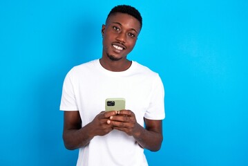 young handsome man wearing white T-shirt over blue background Mock up copy space. Using mobile phone, typing sms message