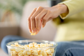 Wall Mural - Young asian woman is grabbing popcorn in a bowl and holding coffee cup while sitting on the big comfortable