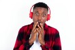 © Jihan - Shocked young handsome man wearing plaid red overshirt over white background stares fearful at camera keeps mouth widely opened wears wireless stereo headphones on ears