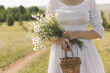 © junky_jess - Faceless woman in vintage white dress walking along a rural road with a bouquet of daisies and a basket in hand in summer, selective focus.