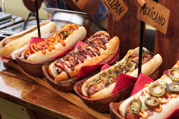 Many hot dogs with various toppings and sauces. Grilled hot dog sausage in a fresh bun. Spicy hot dog with jalapeno, hot dog with mustard. Street food from the food truck festival.