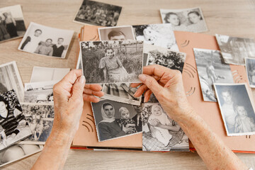 Senior woman is looking her own old photos at home. Elderly woman has got smile while remembering how young and beatiful she was. Selective focus. Photo was taken in 1953