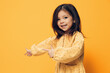 a happy, funny little girl of preschool age stands on an orange background in a trendy dress and points her fingers at the empty space of the background.
