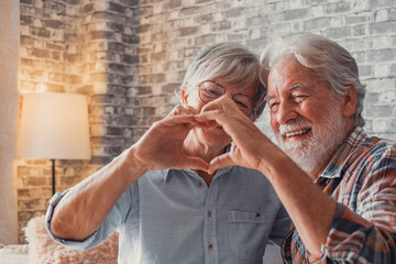 Wall Mural - Close up of hands of two mature grandparents making a heart shape with their fingers together. Smiling and having fun in love people.