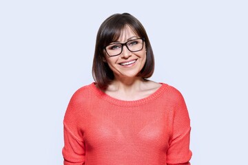 Wall Mural - Smiling middle aged female looking at camera on light studio background