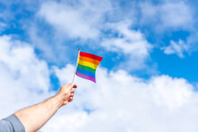 Hand Raised Up With An Unfurled LGBT Flag On A Blue Background