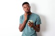 © Jihan - Image of a thinking dreaming young handsome man wearing green T-shirt over white background using mobile phone and holding hand on face. Taking decisions and social media concept.
