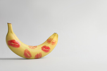 Wall Mural - Banana covered with red lipstick marks on light grey background, space for text. Potency concept