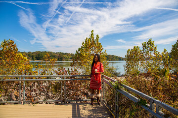 Wall Mural - an African American woman with long sisterlocks wearing an orange dress standing on a wooden platform on the banks of the Tennessee River surrounded by autumn colored trees and lush green trees