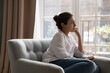 © fizkes - Sad upset young Indian woman thinking while sit on armchair and staring out window. Personal troubles and break up, goes through difficult life situation, search solution, ponders seated alone at home