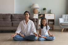 Silent Indian Woman And Preschooler 5s Serene Daughter Meditating Seated In Lotus Position On Warm Floor In Modern Living Room. Good Life Habit, Healthy Lifestyle, Yoga Practice With Children At Home