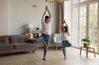 © fizkes - Full-length Indian mum and preschooler daughter in casual wear practicing Tree asana or Vrksasana standing together in cozy warm living room. Beginner yoga work out at home, good life habit, lifestyle